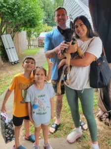 Freya, a Purple Pups GSD German Shepherd puppy, being held by her new owner in a family photo with two adults and two children.